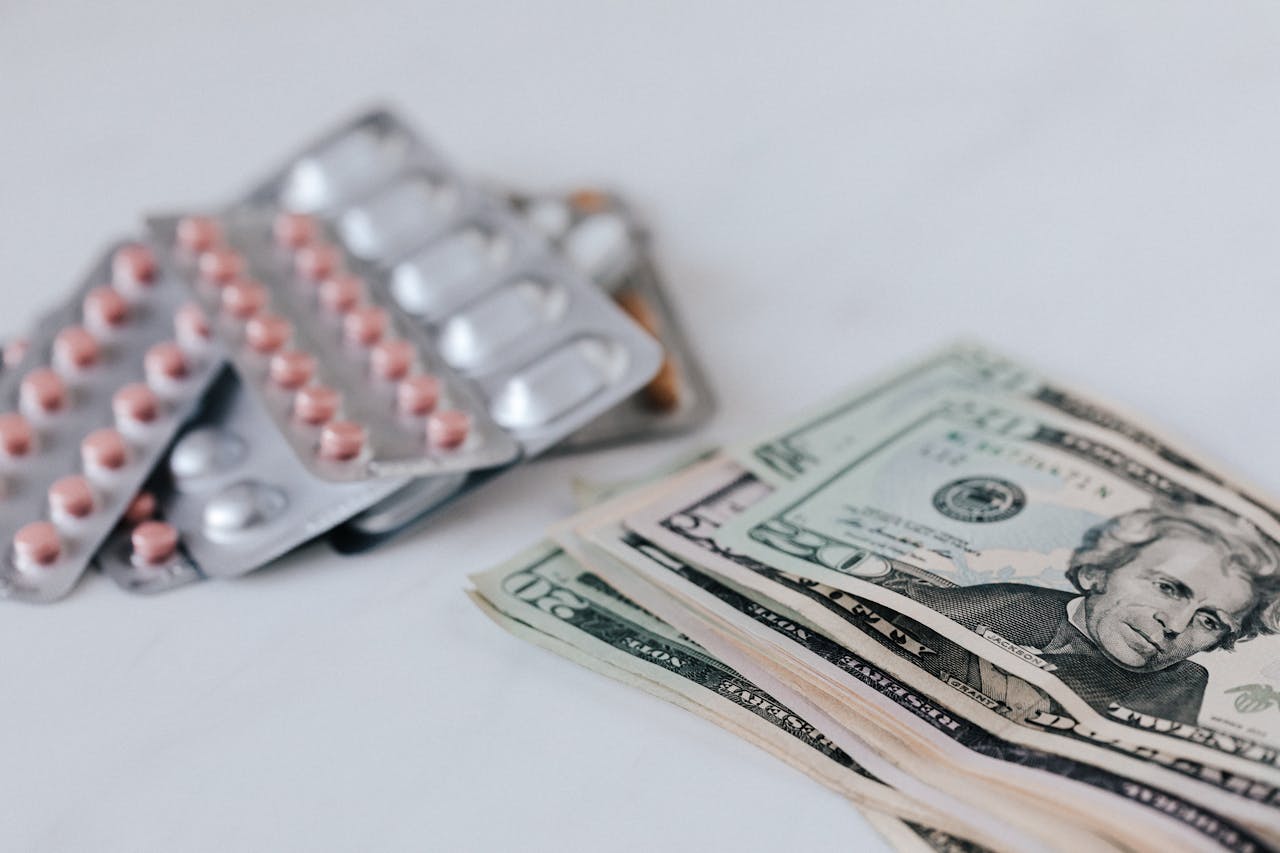 Heap of similar American dollars in cash placed near blisters of expensive drugs on white table